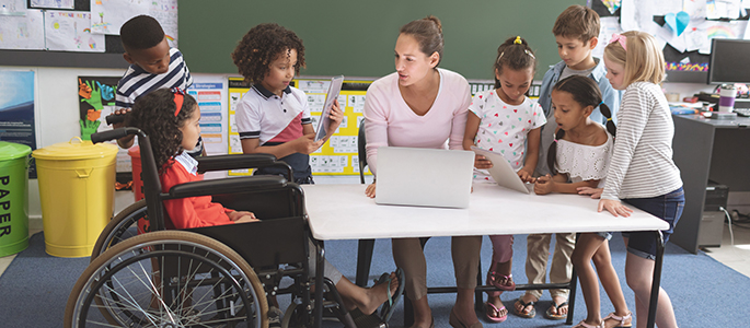 School kids using digital tablet while teacher interacting with students at school