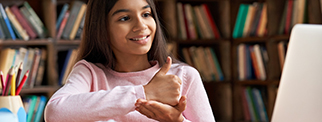 Smiling schoolgirl learning online class on laptop communicating with teacher by video conference call using sign language showing hand gesture during virtual lesson