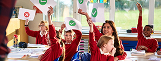 Primary school class holding up pieces of paper, classroom discussion, making decisions, voting