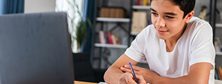 Young boy writing down notes from his laptop